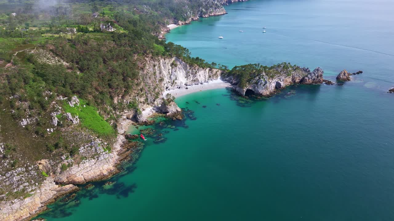 Drone flying forward towards Île Vierge Beach in Crozon Peninsula, Brittany, showing cliffs, turquoise sea, small boats, light mist, and coastal landscape - France