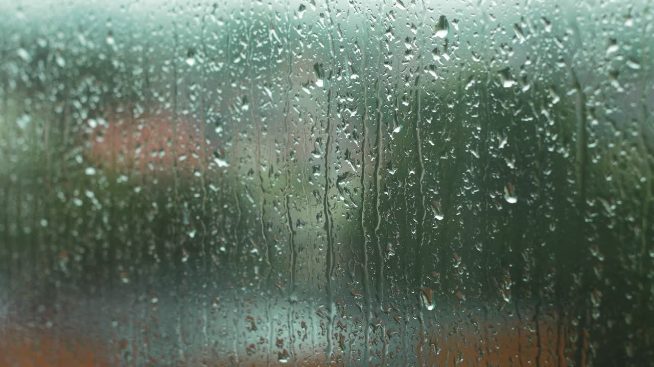 Rain drops sliding slow on window glass in rainy day, de-focused city in background,medium closeup shot