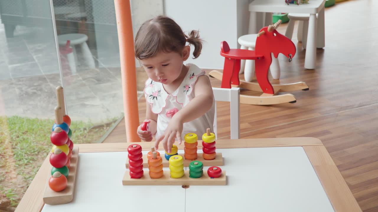 niña en edad preescolar aprendiendo a contar, clasificar y colorear apilando anillos de colores en postes