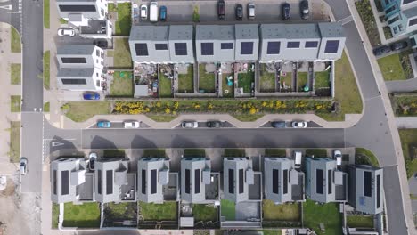 aerial push-in over modern solar-equipped housing row with flat roofs, minimalist facades, landscaped gardens and off-street parking expressing energy-efficient suburban living