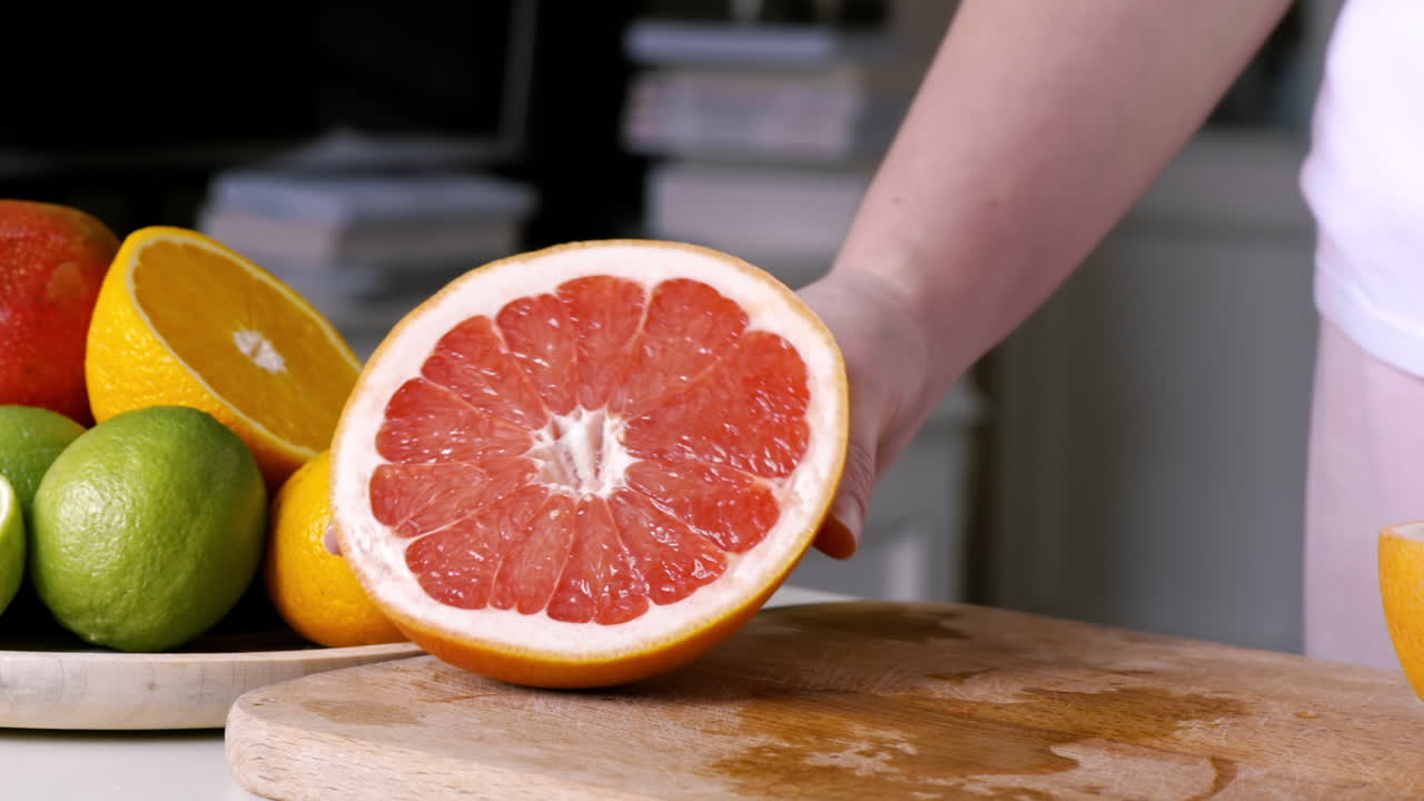 Woman showing cutted part of a grapefruit on a wooden board. Fruits on the background. Slow motion