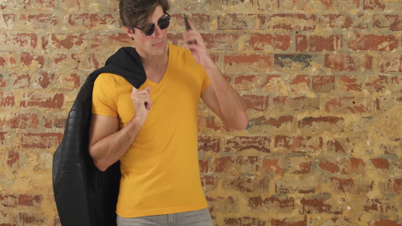 hombre caucásico usando un teléfono inteligente en una pared de ladrillo