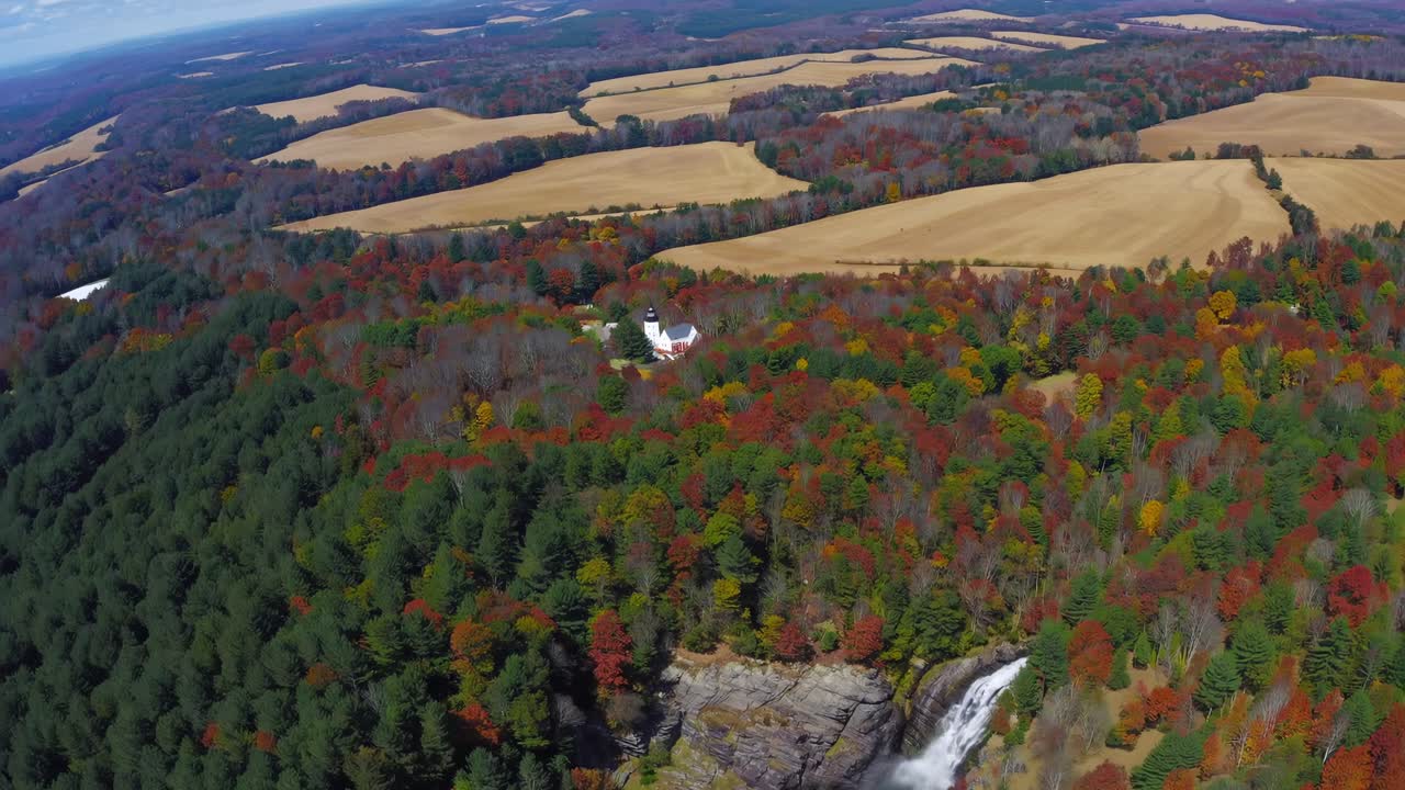 Aerial video captures a vibrant autumn landscape with cascading waterfall and distant fields