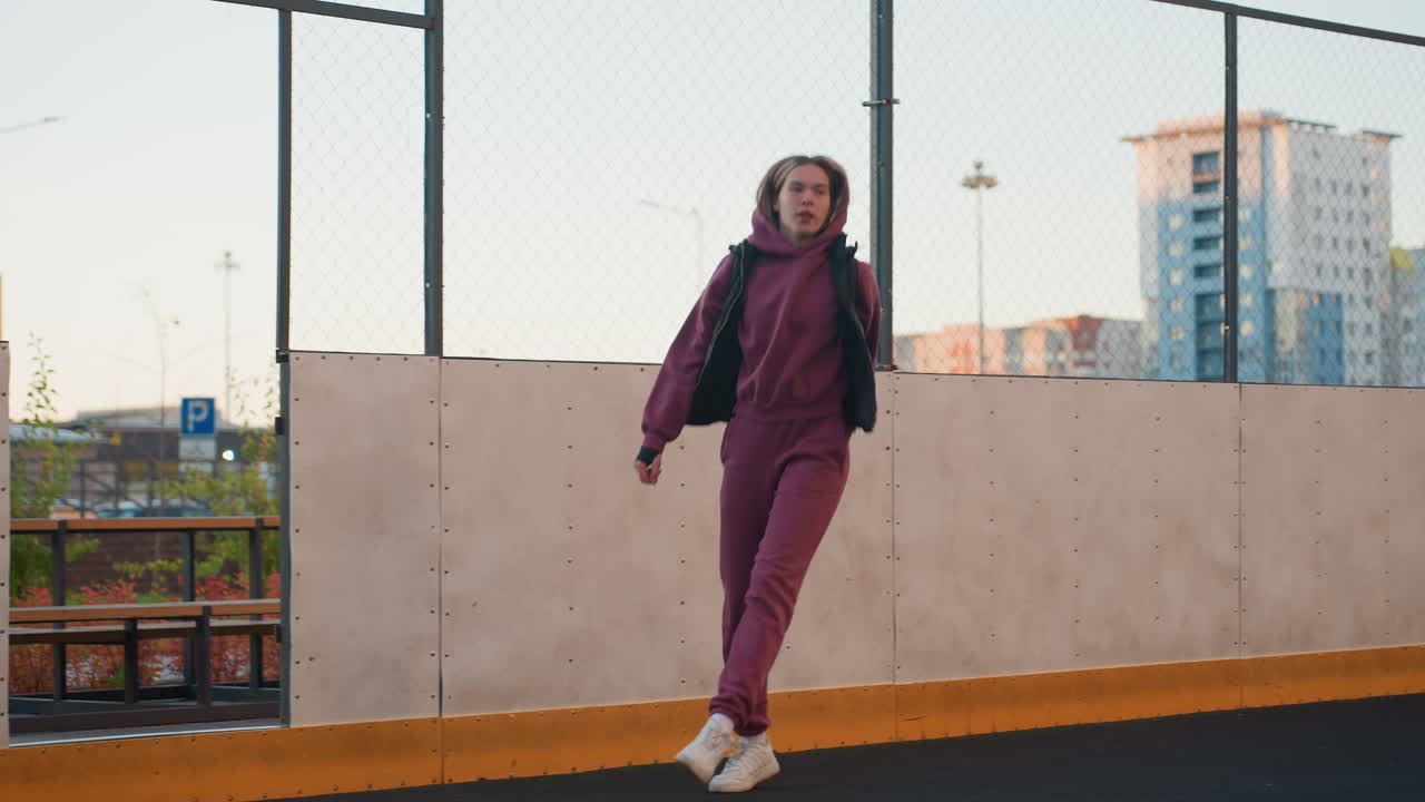Fitness devotee jogging round sports court in urban setting surrounded by modern high rise residential towers under clear sky maintaining steady pace focused on form and rhythm while moving forward