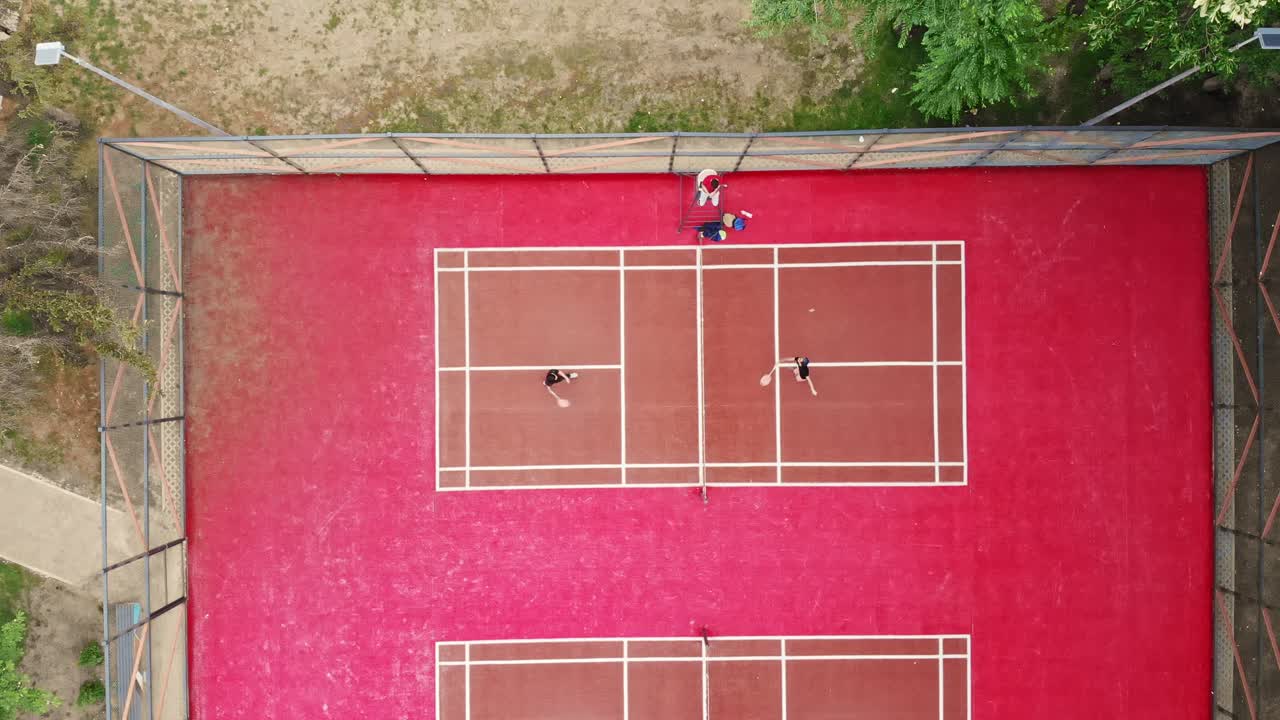 Young guys play badminton on a red court near the forest