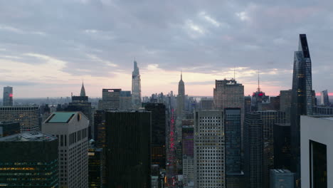 Aerial-descending-footage-of-downtown-business-skyscrapers-at-dusk.-Busy-long-straight-avenue-with-distinctive-red-row-of-brake-lights.-Manhattan,-New-York-City,-USA