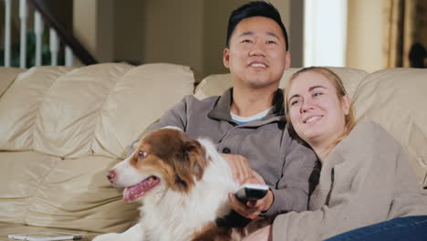 young loving couple with dog sit on the couch watching tv