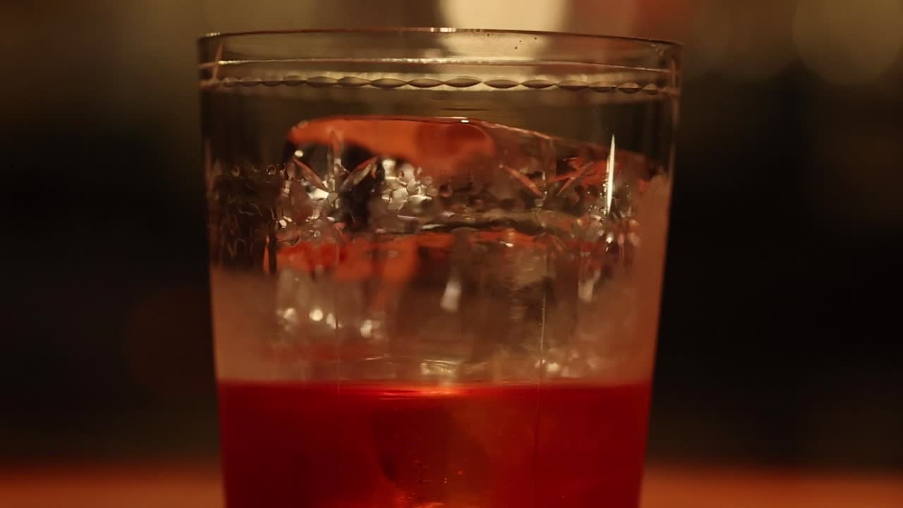 A detailed view of ice cubes floating in a red drink, with a hand adjusting the glass.