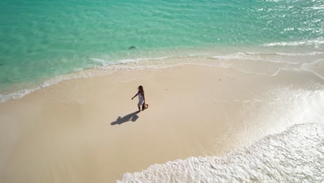 aerial view woman in white dress and straw hat in hands on beautiful deserted beach