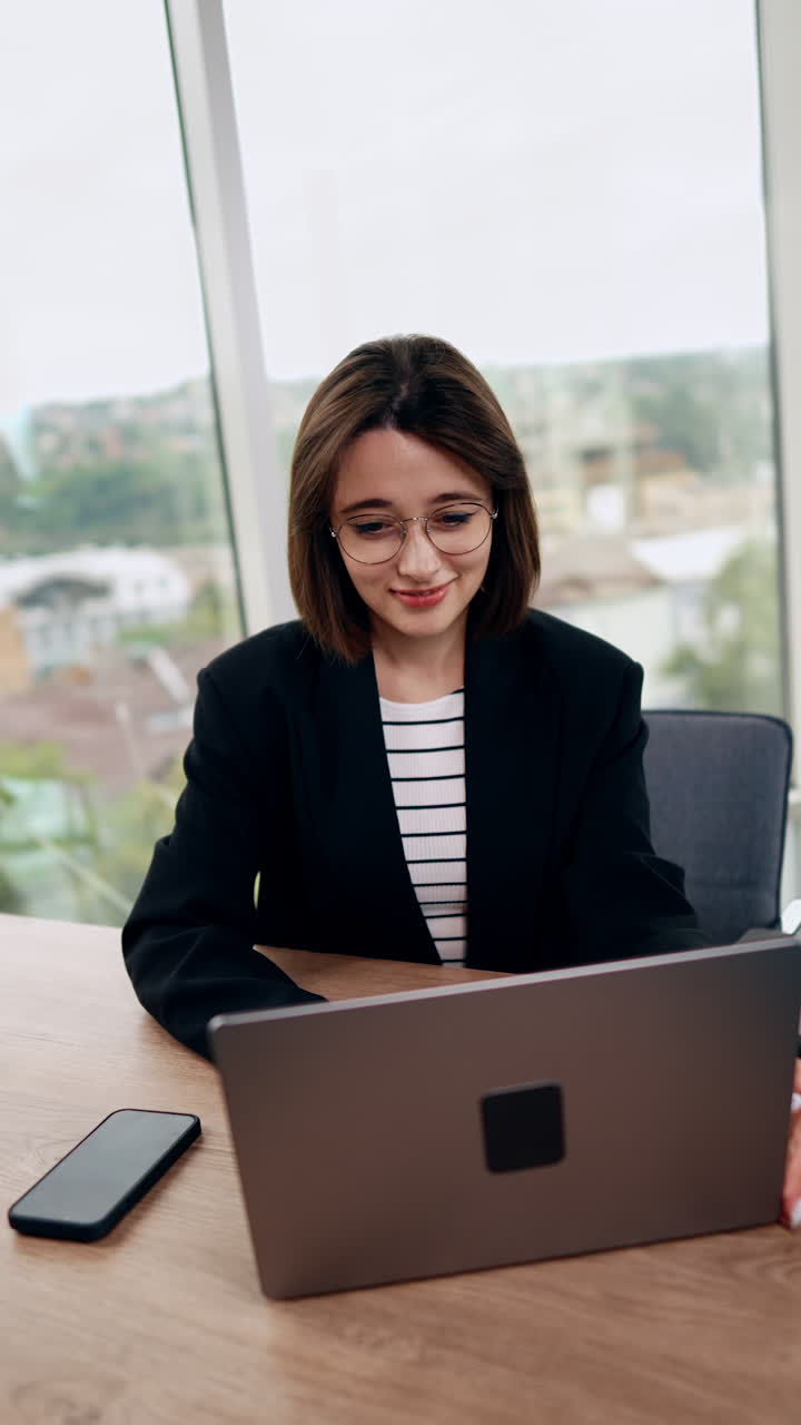 Confident resilient lady working at laptop in the office. Portrait of a confident modern businesswoman at her working place. Vertical video.
