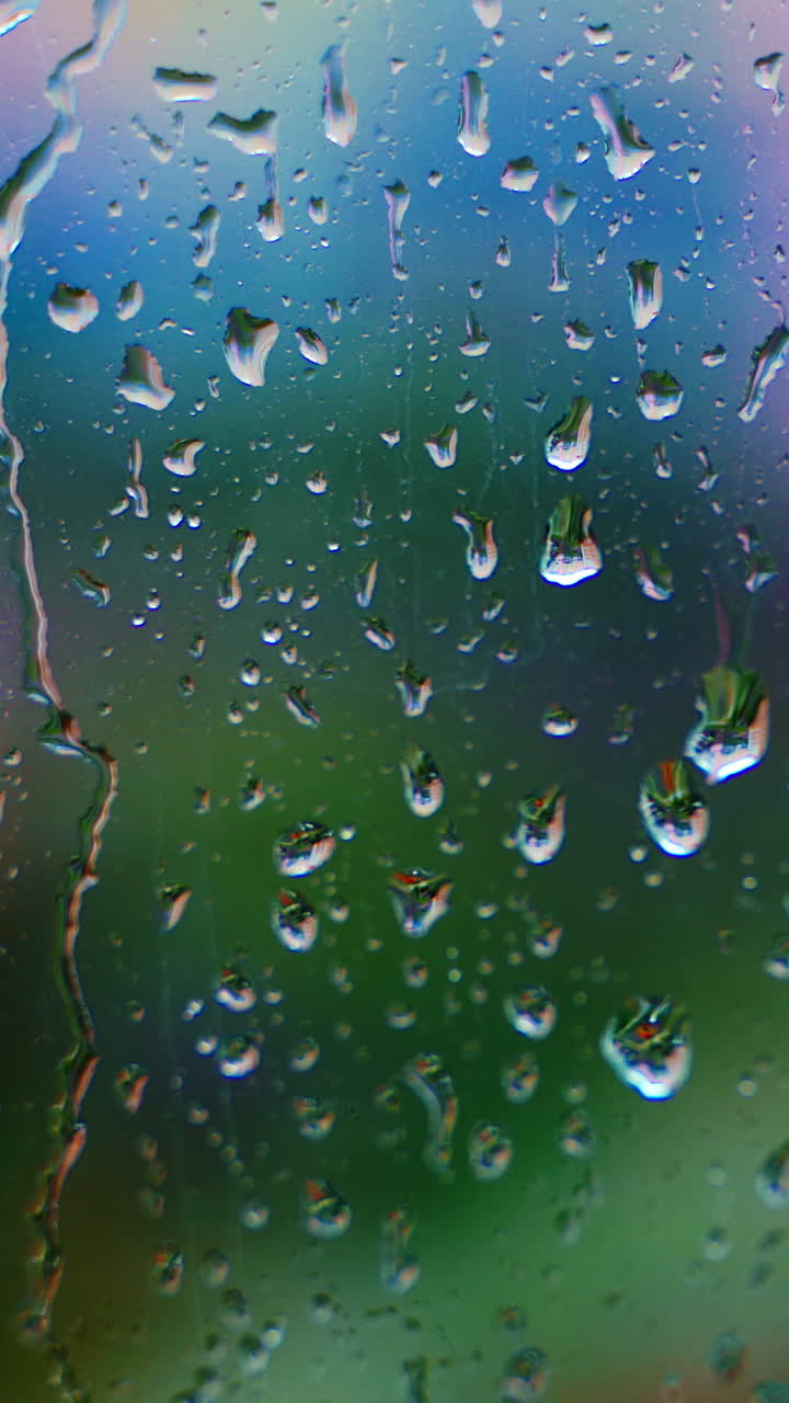 Drops of rain on window glass on blur background. Rainy weather. Rain droplets flowing down on glass window at rainy day. Close-up. Vertical video