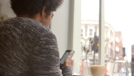 joven usando un teléfono móvil para actualizar las redes sociales en un café