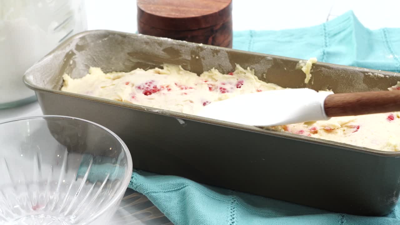 Making a dessert called Red Raspberry Tea Cake made with fresh berries and vanilla buttercream frosting. Great for Tea Parties. Spreading out the vanilla cake batter in the baking loaf pan to bake