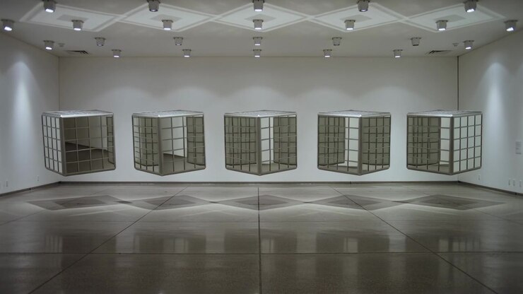 Rotating five suspended grid cubes syncing in gallery under spotlights, shifting floor reflections