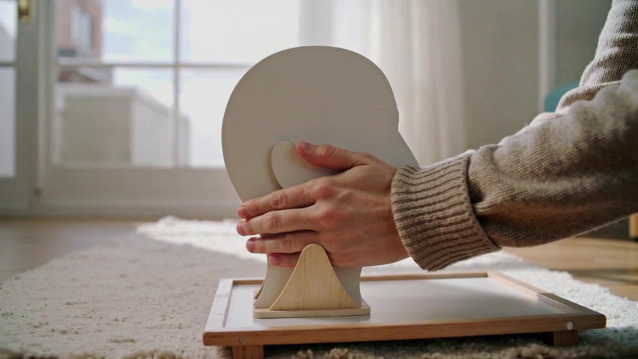Entering hands in ribbed sweater lowering wooden head onto cradle on board, aligning peg, mounting