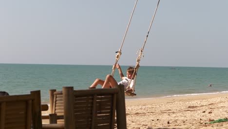 cámara lenta de niño en columpio de árbol en playa tropical, horizonte oceánico en segundo plano