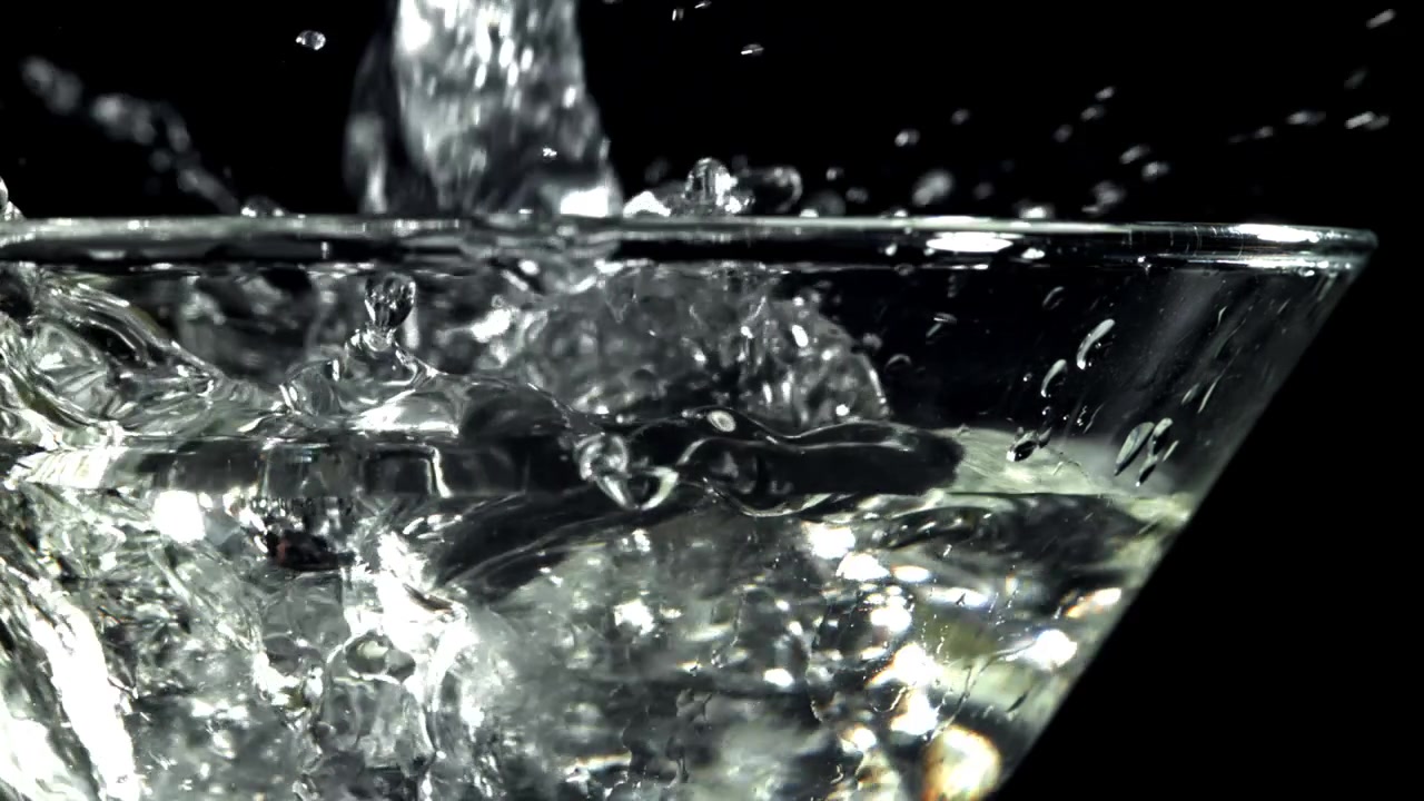 Cubetti di ghiaccio che schizzano in un bicchiere d'acqua trasparente al rallentatore