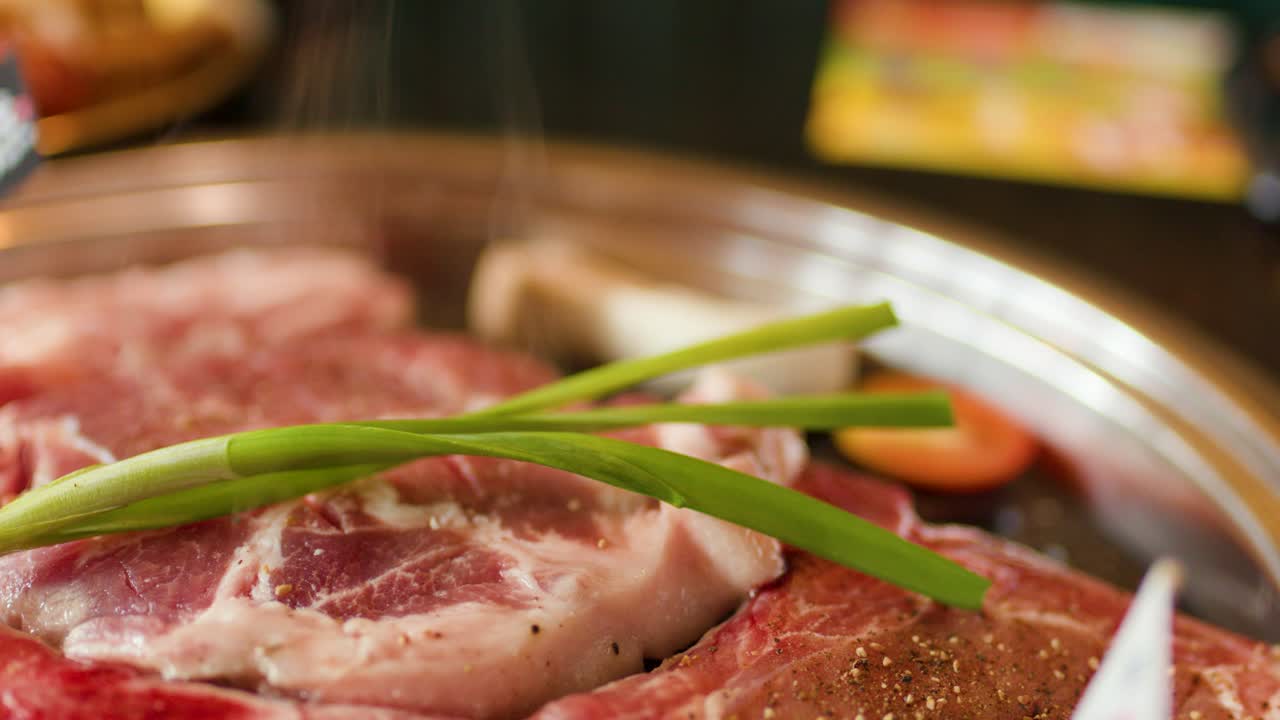 Raw beef and vegetables sizzle on a hot grill pan, steam rising in warm light