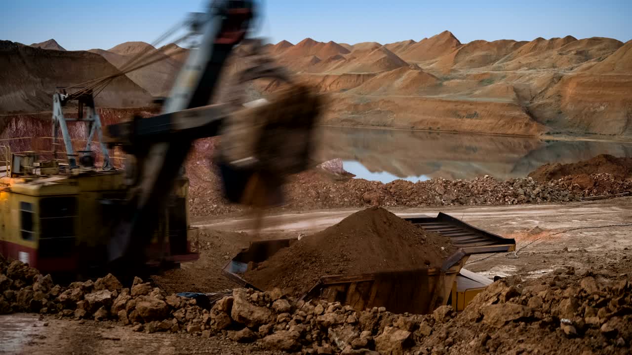 Time lapse of excavator loading ore into dump-trucks at the sunset.