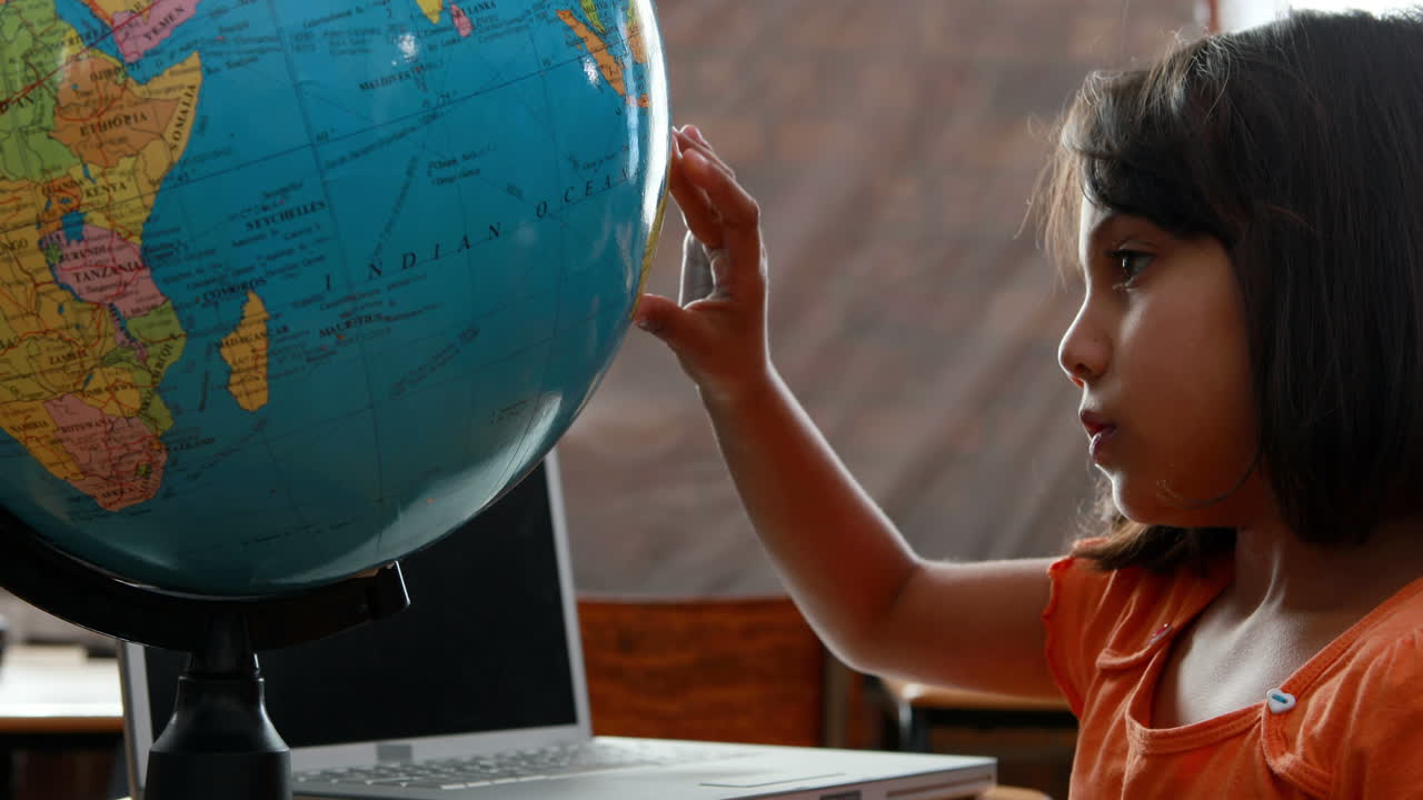 Little girl looking at globe in classroom
