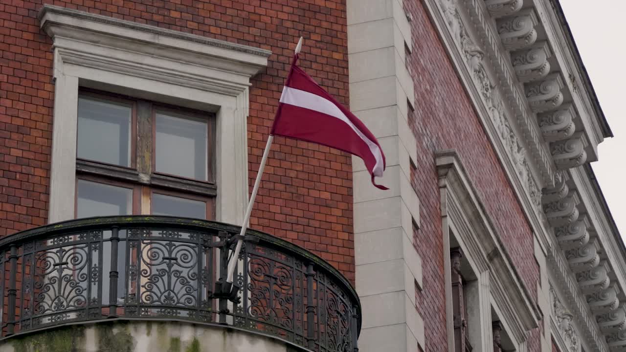 Locked off view of Latvian flag waving on balcony of brick building