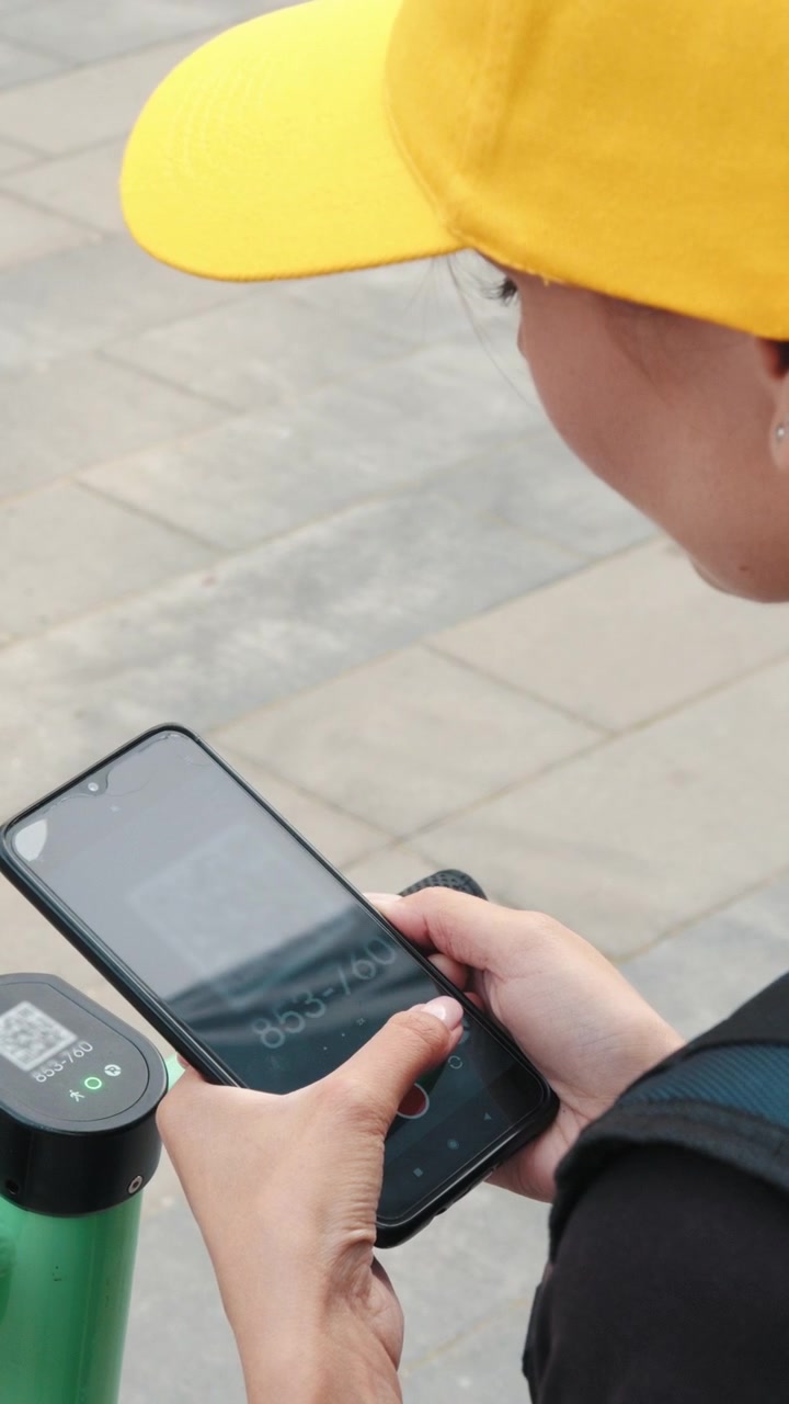 Una persona con gorra amarilla escanea un código QR en su teléfono para desbloquear un patinete eléctrico mostrando.