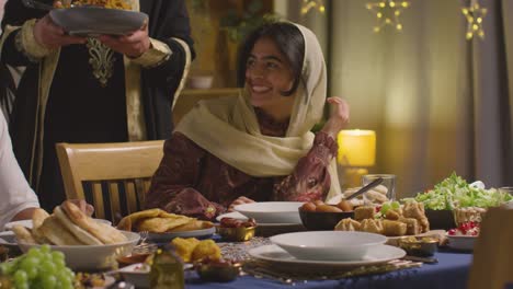 Muslimische-Familie-Sitzt-Zu-Hause-Am-Tisch-Mit-Einer-Frau,-Die-Biryani-Beim-Essen-Serviert,-Um-Eid-Zu-Feiern
