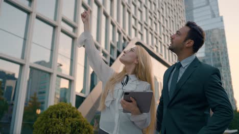 two businesspeople using a digital tablet together in the city outside business building, woman pointing hand up showing something to man