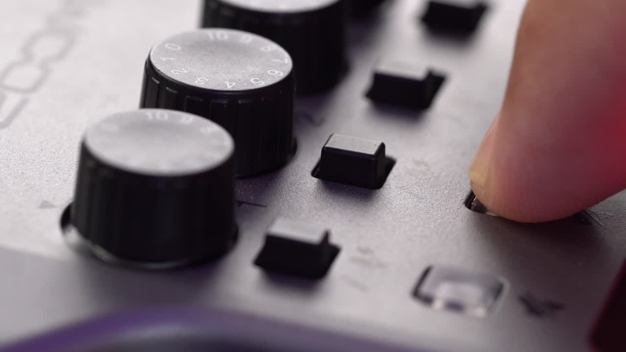 Macro shot of a hand pressing a button on a black audio mixer, showing dials and controls in sharp detail