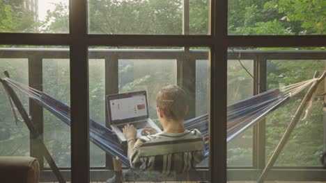 Rear-View-Of-A-Man-Using-Laptop-While-Relaxing-In-A-Hammock