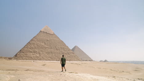 un hombre caminando por la meseta de giza con una vista de las pirámides en el cairo, egipto - toma de avión no tripulado en órbita
