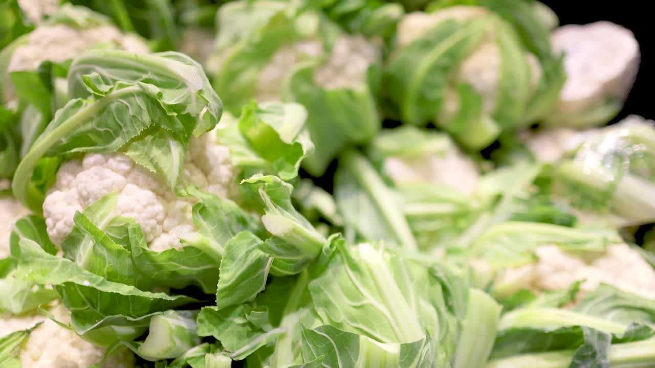 Close-up view of fresh cauliflower heads in a well-lit supermarket setting, highlighting texture and vibrant green leaves