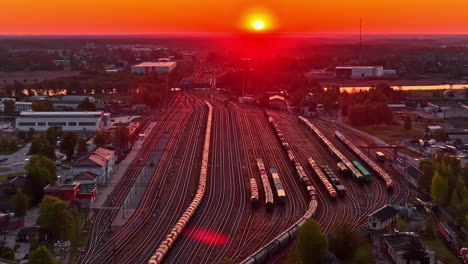 train yard filled with freight cars at sunset under intense red-orange sky in drone video