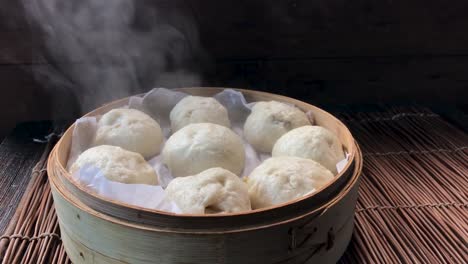 three quarter view of fast uncovering lid of cooked steamed buns showing steam rising