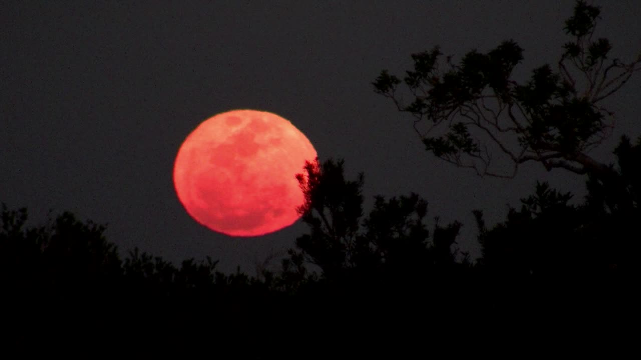 Uma lua laranja surge atrás de um cume