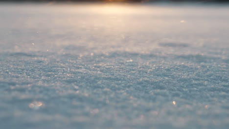 Tiefwinkelaufnahme-Von-Schneekristallen,-Die-In-Der-Abenddämmerung-Im-Wind-über-Schneebedeckten-Boden-Wehen