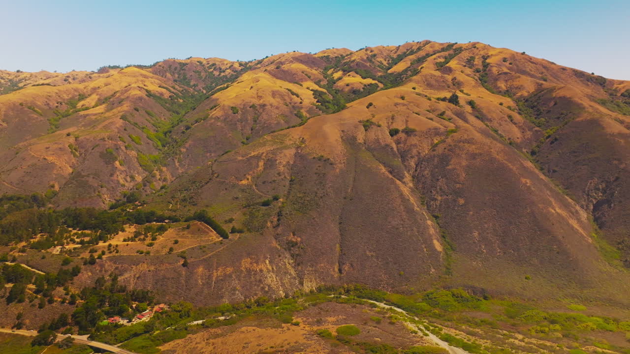 Approaching the sloping bare mountains with scarce vegetation at the foot. Beautiful rocky landscape at the backdrop of clear blue skies.