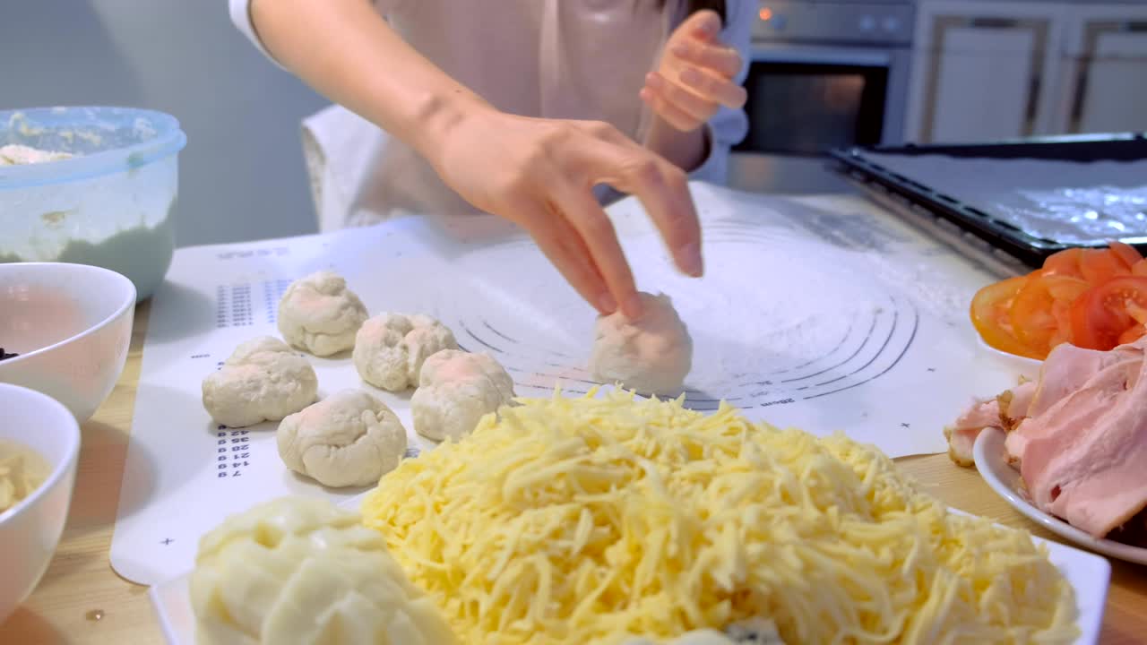 여성이 다른 재료로 피자를 위해 반죽 공을 만니다. 손 클로즈업.