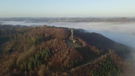 observation tower with transmission mast sitting on the edge of a steep hill in morsbach, germany during sunrise