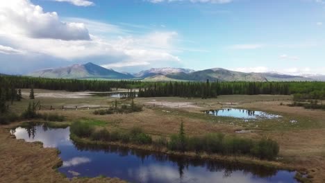 Espectacular-Escena-Panorámica-De-La-Naturaleza-Del-Paisaje-Al-Aire-Libre-Del-Yukón-Y-Vuelo-Sobre-El-Lago-Del-Espejo,-Gran-Cielo-Azul-Expansivo-Y-Cordillera-En-El-Fondo,-Caballo-Blanco,-Canadá,-Enfoque-Aéreo-Superior