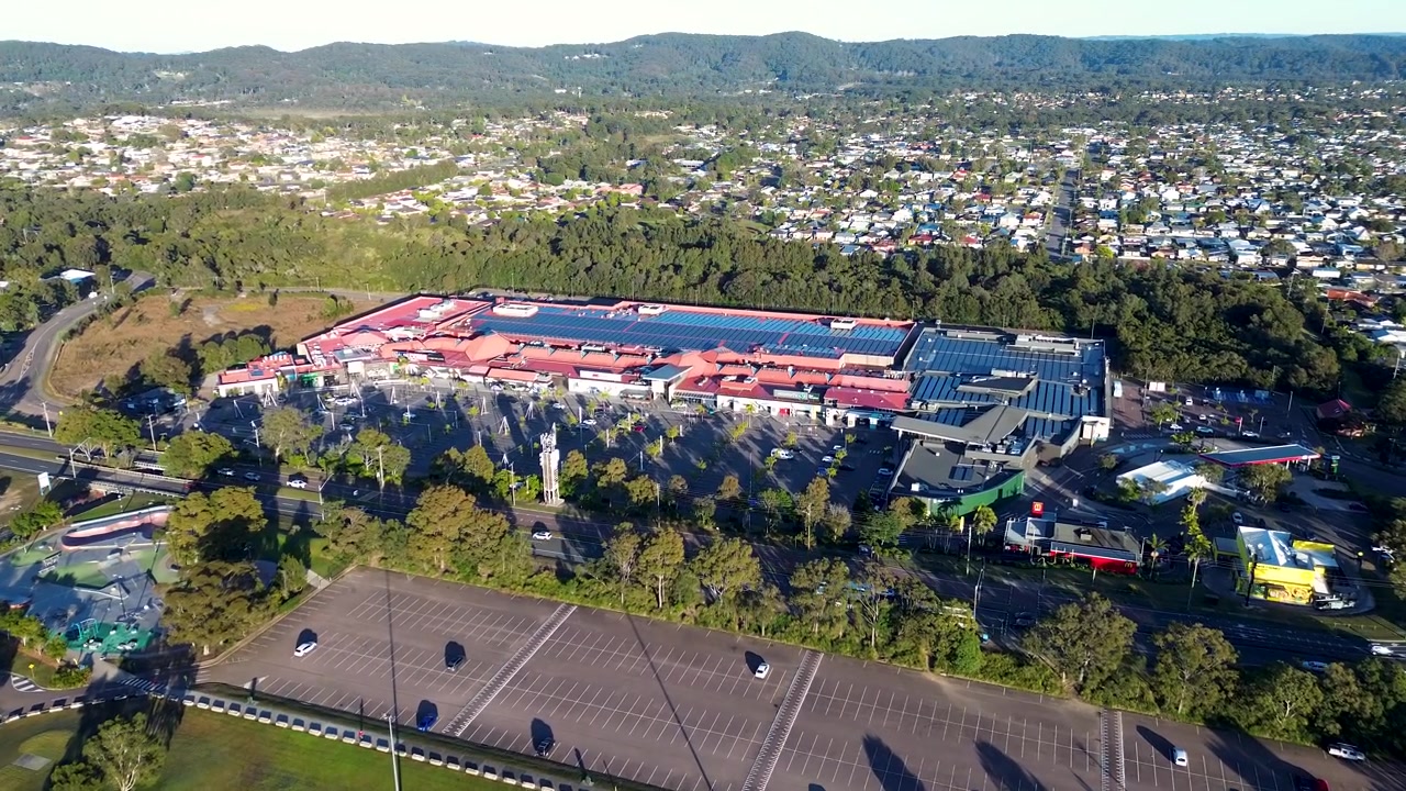 Drohnen-Luftaufnahme der Landschaft des Einkaufszentrums Bateau Bay, umgeben von einem öffentlichen Parkplatz, nahe der Hauptstraße und einem Vorstadtviertel an der Central Coast NSW, Australien
