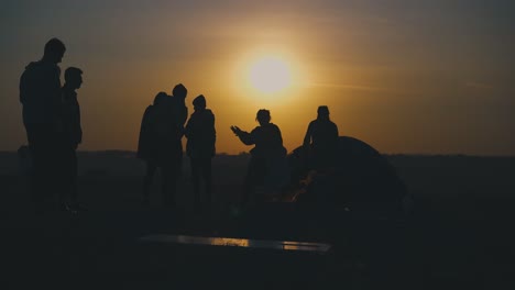 young tourists rest at burning bonfire at sunset time