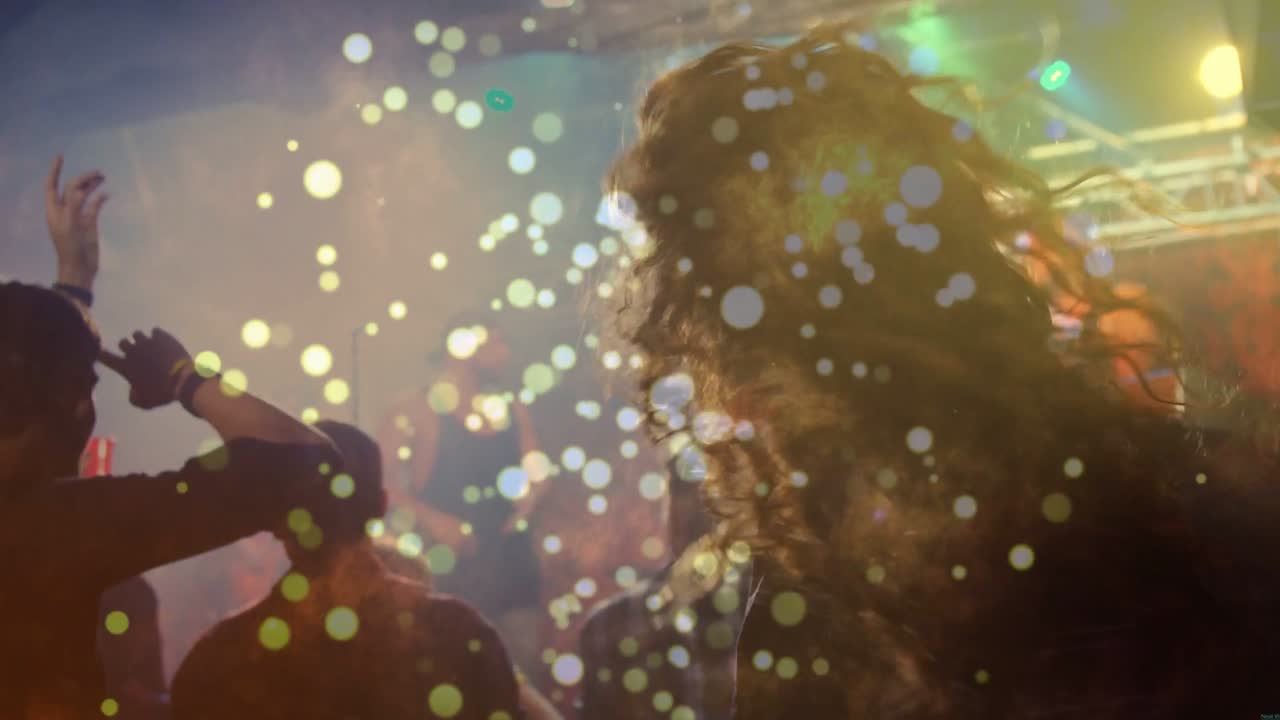 Folla che si muove a musica pulsante, effetto bokeh che fluttua sui volti mentre un fan dai capelli lunghi si gira verso la console.