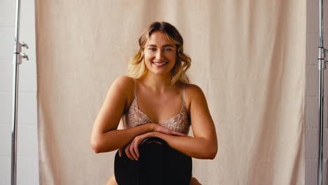 fotografía de estudio de una mujer natural y segura en ropa interior que promueve la positividad corporal sentada en una silla