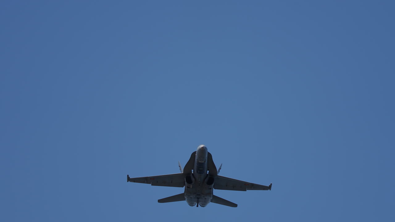 Military jet aircraft flying directly overhead with clear view of engines and wings against blue sky