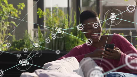 animation of network of connections with icons over african american woman using smartphone