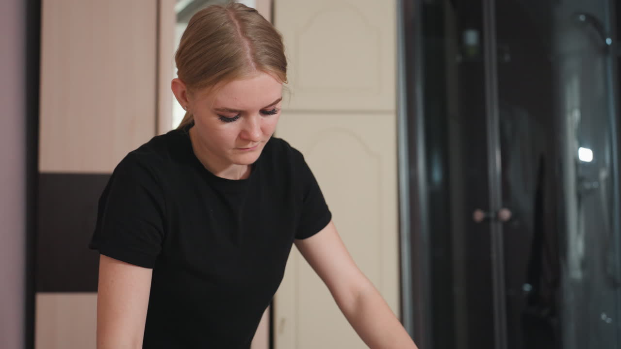 Focused massage therapist wearing black applying technique during wellness treatment in modern spa environment with muted interior colors, shower enclosure, and wooden cabinet visible in background