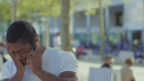 thoughtful african american guy talking on phone and rubbing face.