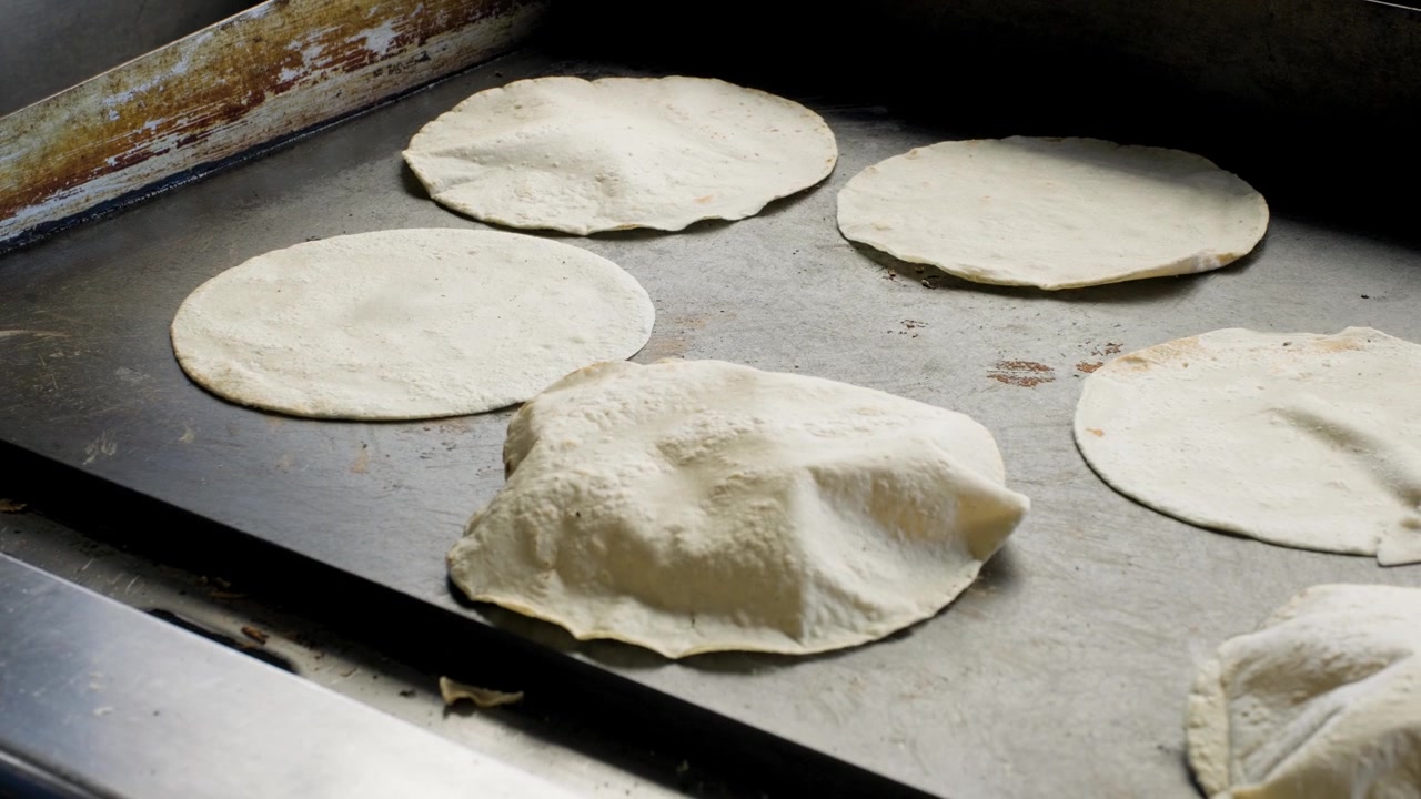 Filmato di cucina tradizionale che mostra una donna che gira le tortillas su una piastra piatta durante la preparazione di tortillas di mais fresche fatte a mano.