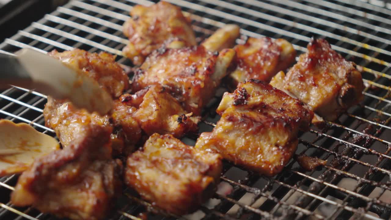 Close up shot of a grill with pork ribs roasting, cook's hand working with tongs